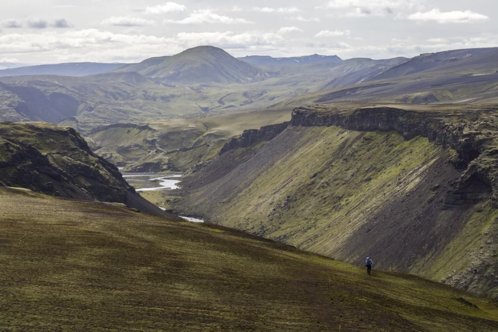 Ein Mensch läuft am Rande einer Schlucht in grau-grüner Berglandschaft