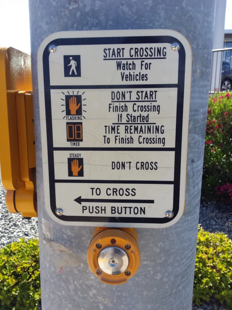 Ein Schild auf einer Ampel, die genau erklärt welches Symbol auf der Fußgängerampel was bedeutet (z. B. gehender Mensch = loslaufen)