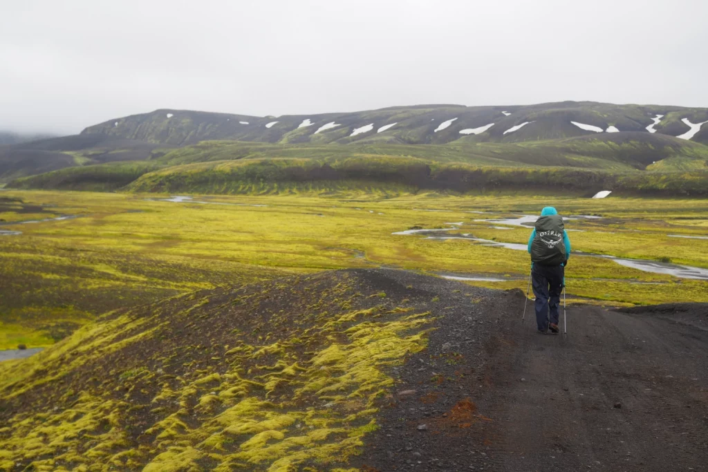 Wanderer auf Schotterpiste in karger grün-grauer Landschaft