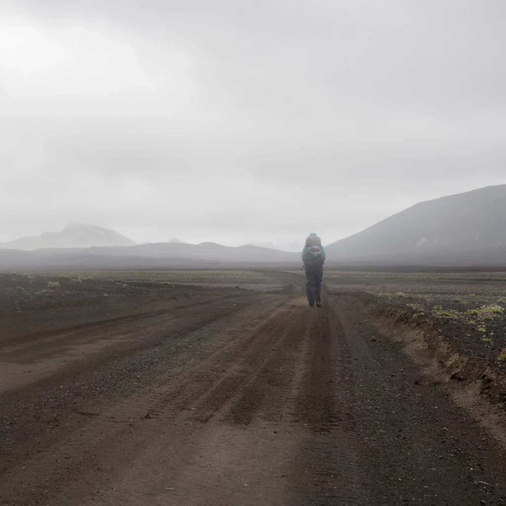 Wanderer auf Schotterpiste in nebliger Regenstimmung in grauer isländischer Landschaft