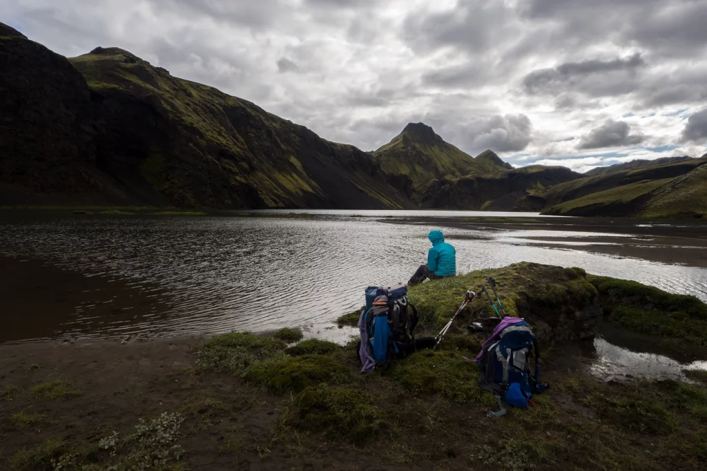 dunkle Bildstimmung, Person sitzt auf einem Fels an einem Bergsee