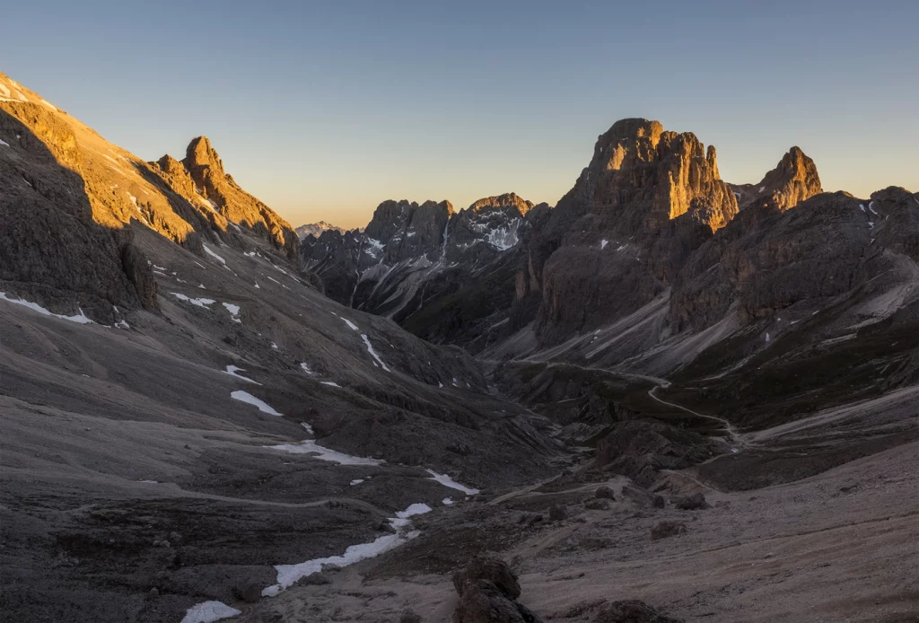 Ein Bergtal, das Tal liegt bereits im Schatten, die Berggipfel sind von der Sonne erleuchtet